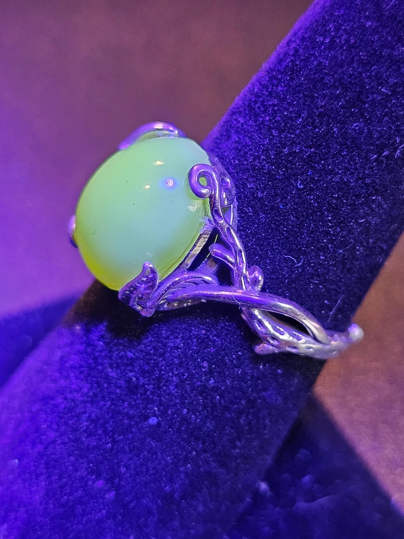 May include: A silver ring with a large, round, pale green gemstone set in a delicate, leafy design.