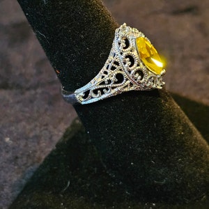 May include: A silver filigree ring with a large, oval-shaped, yellow gemstone.