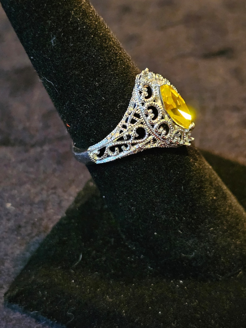 May include: A silver filigree ring with a large, oval-shaped, yellow gemstone.
