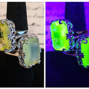 Può includere: Un anello d'argento con due grandi pietre rettangolari giallo chiaro. L'anello presenta un design ornato a filigrana attorno alle pietre. Sotto la luce nera, le pietre preziose brillano di verde brillante.