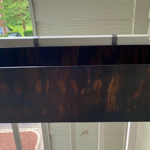 May include: A dark brown wooden planter box with a slightly angled design, hanging from a white railing.