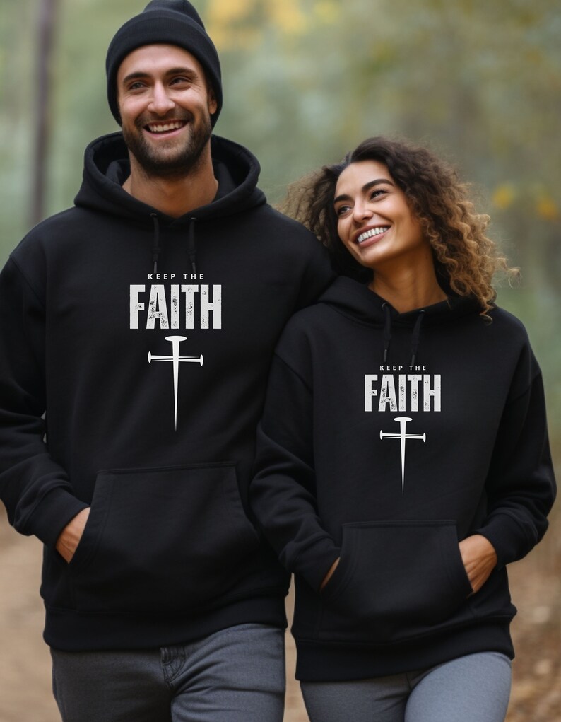 Op de afbeelding: Twee zwarte hoodies met de tekst "Keep the Faith" en een gestileerd kruis met een spijkerontwerp in wit.