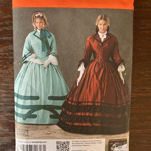 May include: Simplicity sewing pattern 1818 KK featuring two women in historical dresses. The pattern includes sizes US 8-14. The dresses are in shades of teal and rust, with white accents. The pattern's brand name is Simplicity.