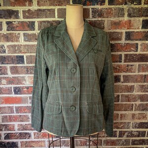 May include: A long-sleeve blazer in a muted olive green with a subtle brown and light green plaid pattern. The garment features a notched lapel, three matching olive green buttons down the front, and two flap pockets at the lower front section.