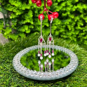 May include: A pair of silver dangle earrings with a geometric design. The earrings feature pink gemstones and white pearls.