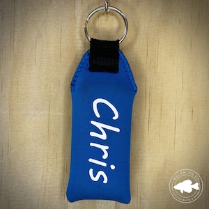May include: A blue neoprene key chain with a white inscription that reads "Chris".