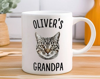 May include: White ceramic mug with a black and white image of a cat and the text "Oliver's Grandpa" printed on it.