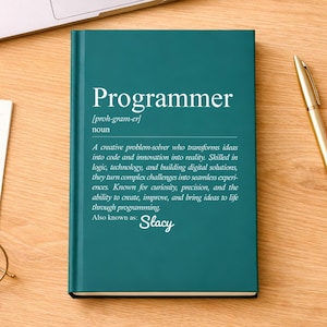 May include: A teal book titled "Programmer" with a definition, a laptop, a pen, sticky notes, a computer mouse, and glasses on a wooden desk. The book's definition describes a creative problem-solver.