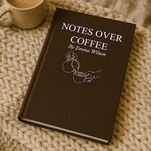 May include: A brown book titled "NOTES OVER COFFEE" by Emma Wilson, with a coffee cup illustration, rests on a cream-colored knitted blanket. A mug of coffee and a lit candle are also present, creating a cozy atmosphere.