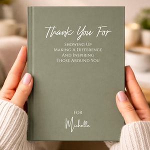 May include: A sage green hardcover journal with white text that reads: Thank You For SHOWING UP MAKING A DIFFERENCE AND INSPIRING THOSE AROUND YOU FOR Michelle. The book has a smooth matte finish and a vertical spine detail on the left side.