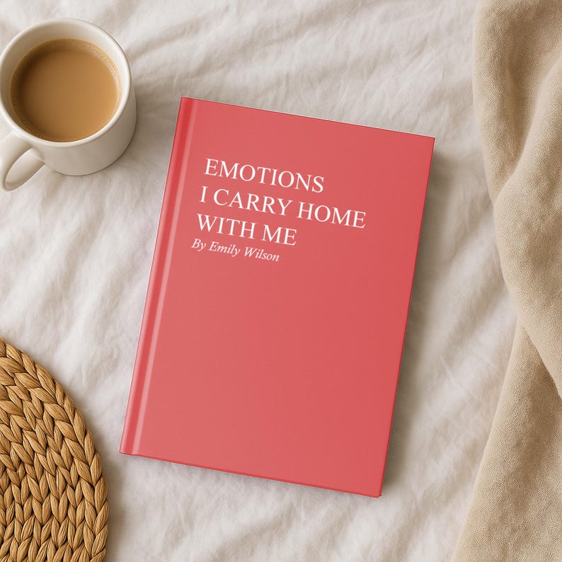 May include: A coral-colored book titled "EMOTIONS I CARRY HOME WITH ME" by Emily Wilson. A white mug filled with coffee sits to the left of the book. The book and mug are on a white, textured surface.