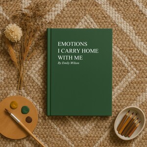 May include: A hardcover book with the title "EMOTIONS I CARRY HOME WITH ME" by Emily Wilson. The book is dark green and sits on a patterned rug, next to a wooden palette with paint, a paintbrush, and a small bowl of pencils.