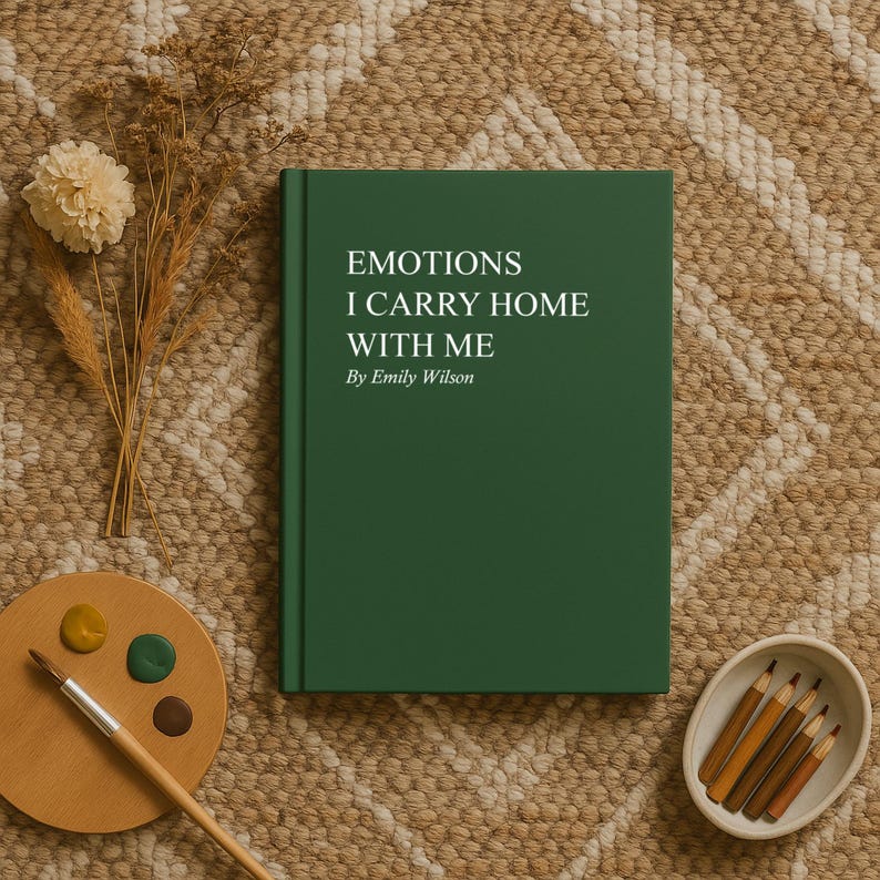 May include: A hardcover book with the title "EMOTIONS I CARRY HOME WITH ME" by Emily Wilson. The book is dark green and sits on a patterned rug, next to a wooden palette with paint, a paintbrush, and a small bowl of pencils.