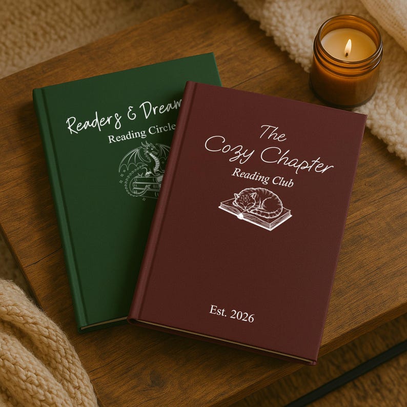 May include: Two hardback books with text and illustrations. One is dark green with "Readers & Dream Reading Circle" and a dragon illustration. The other is burgundy with "The Cozy Chapter Reading Club" and a cat illustration. A lit candle is nearby.