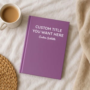 May include: A purple hardcover book with the text "CUSTOM TITLE YOU WANT HERE" and "Custom Subtitle" in white. A cup of coffee sits to the left of the book, and a woven coaster is in the lower left corner.