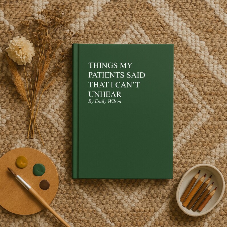 May include: A hardcover book with a dark green cover, titled "THINGS MY PATIENTS SAID THAT I CAN'T UNHEAR By Emily Wilson." The book is on a textured, neutral-toned surface, with a palette, paint brush, and pencils.