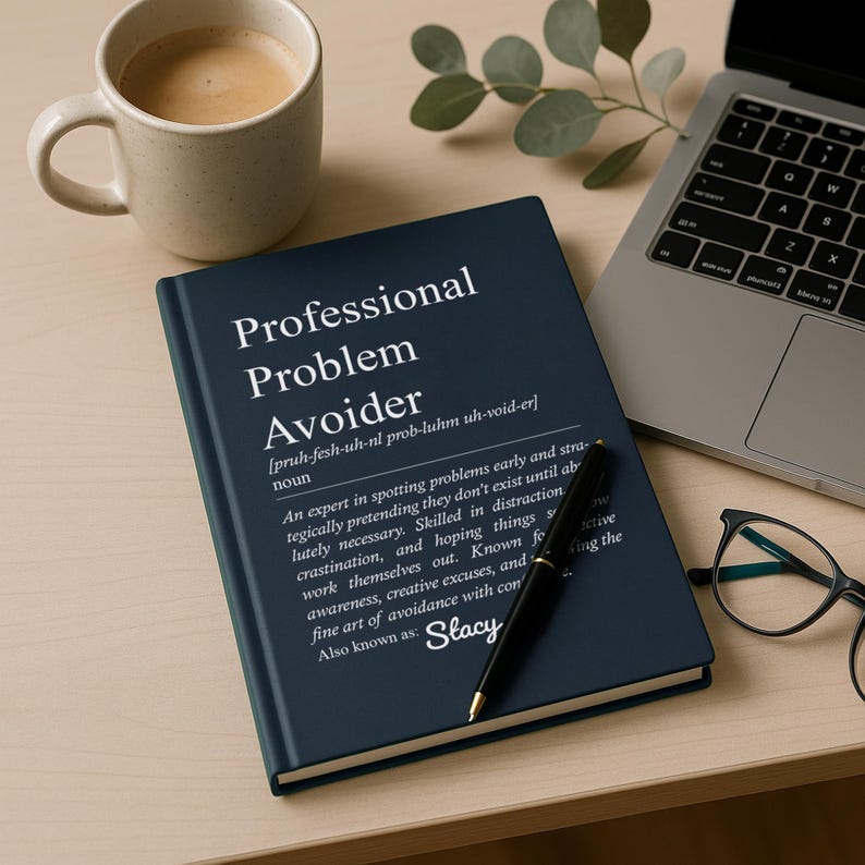 May include: A navy blue notebook with the words "Professional Problem Avoider" in white. A black pen rests on the notebook, and a cup of coffee and a laptop are in the background.