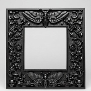 May include: Square black mirror with ornate carved frame. The frame features moth and skull motifs, floral elements, and crescent moons. The mirror is a decorative gothic-style home decor item.