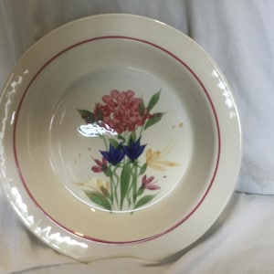 May include: A white ceramic pie plate with a red rim and a floral design featuring pink, blue, and yellow flowers.