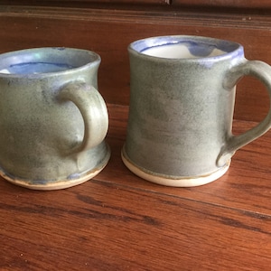 May include: Two ceramic mugs with a blue and green glaze. The mugs have a rounded shape and a handle.