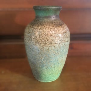 May include: A small, green and brown ceramic vase with a speckled glaze.
