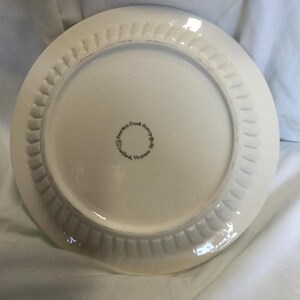 May include: White ceramic plate with a scalloped edge. The bottom of the plate has the text "James Creek Pottery, Stafford, Virginia" printed in black.