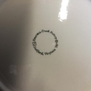 May include: A white ceramic plate with a black stamp that reads "Emerson Creek Pottery, Bedford, Virginia 1996".