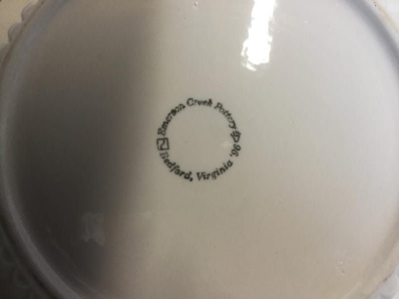 May include: A white ceramic plate with a black stamp that reads "Emerson Creek Pottery, Bedford, Virginia 1996".