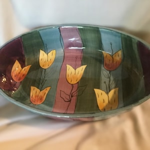 May include: An oval ceramic serving dish with a colorful striped design featuring yellow, orange, green, purple, and blue. The dish is decorated with hand-painted stylized tulips.