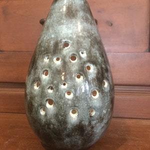 May include: A teal and black ceramic vase with a teardrop shape and a pattern of small holes. The vase is glazed and has a glossy finish.