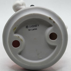 Op de afbeelding: Witte keramische figuur van Mickey Mouse met zwarte oren en een rode broek. De onderkant van de figuur heeft een witte cirkel met de tekst "&copy; DISNEY Sri Lanka".