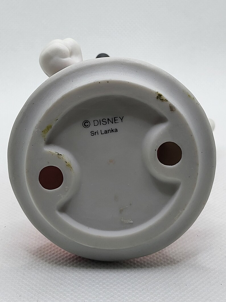Op de afbeelding: Witte keramische figuur van Mickey Mouse met zwarte oren en een rode broek. De onderkant van de figuur heeft een witte cirkel met de tekst "&copy; DISNEY Sri Lanka".