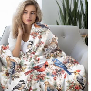 May include: A white throw blanket with a colorful bird and berry pattern. The blanket features a variety of birds, including cardinals, bluebirds, and robins, as well as red berries and pine cones.