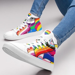 Może przedstawiać: Białe, wysokie buty z płótna z kolorowym wzorem tęczowej flagi dumy. Buty mają białe sznurówki i białą gumową podeszwę.