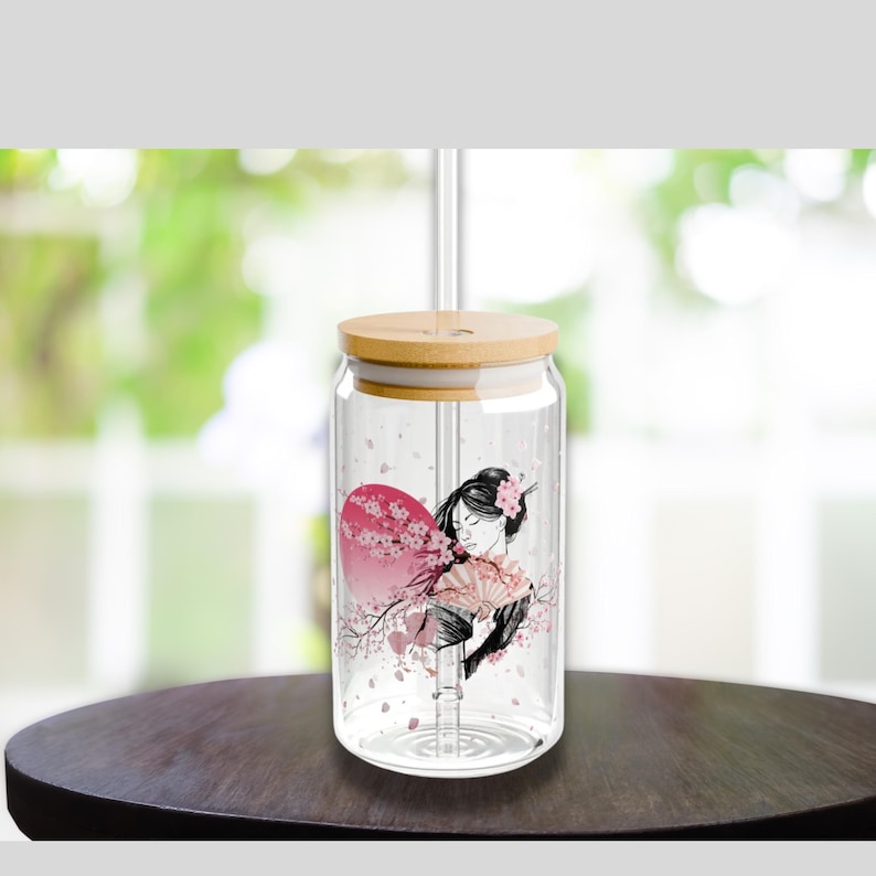 May include: A clear glass jar with a bamboo lid and a straw. The jar has a design of a woman with a fan and cherry blossoms.