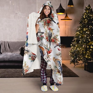 Puede incluir: Una manta con capucha con un exterior blanco con un diseño de acuarela de pájaros, bayas rojas y follaje verde. El interior es de material sherpa suave color crema. La manta está diseñada para ser usada.