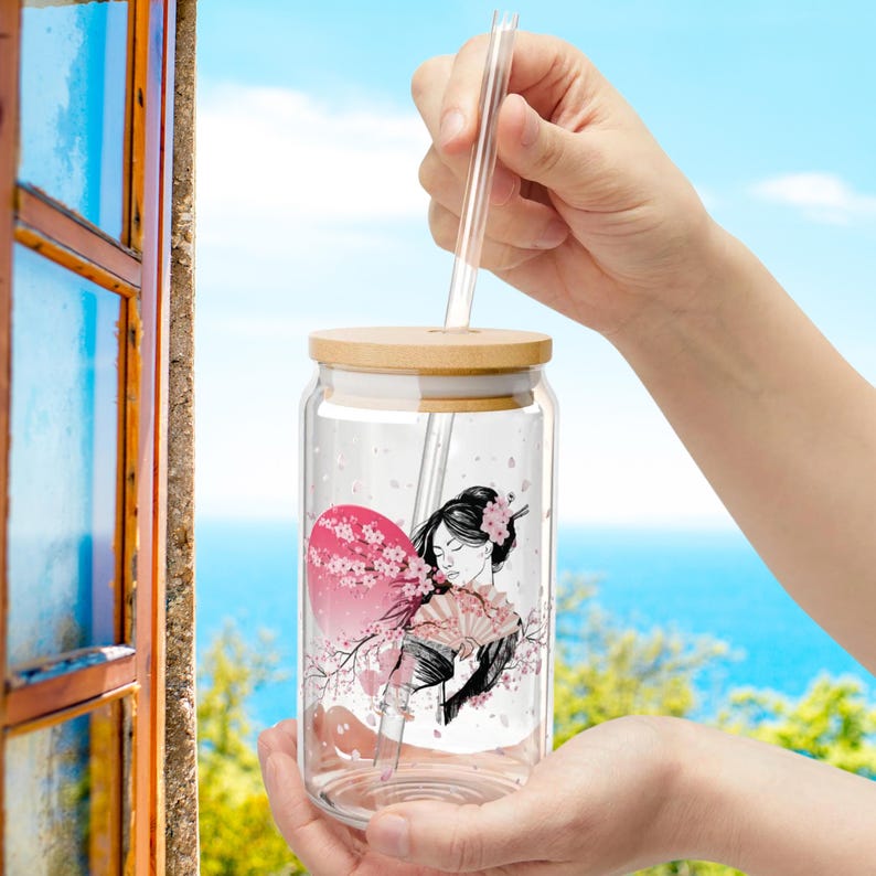 May include: A glass jar with a bamboo lid and a straw. The jar has a design of a woman with a fan and cherry blossoms.