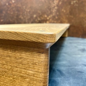 Könnte beinhalten: Ein Holzsockel mit natürlicher Oberfläche. Der Sockel hat eine rechteckige Oberseite und eine leicht abgerundete Basis. Die Holzmaserung ist auf der Oberfläche sichtbar.