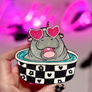 May include: A white ceramic mug with a black handle and the text "But First, Coffee" in a bold, black font. The mug is set against a neutral background, highlighting its simple design.