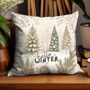May include: A decorative square pillow with a winter forest scene. The pillow features a cream-colored background with illustrations of pine trees, pine cones, and the text "hello WINTER". The pillow is approximately 18 inches square.