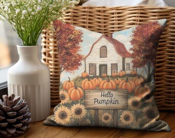 May include: A decorative throw pillow with a fall-themed design. The pillow features a white farmhouse with a red roof, surrounded by pumpkins and sunflowers. The text "Hello Pumpkin" is displayed on a wooden sign in front of the house.
