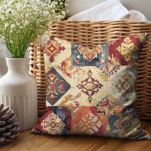 May include: Square decorative pillow with a patchwork design. The pillow features geometric patterns in shades of red, blue, yellow, and cream. The pillow is placed on a wooden surface.