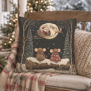 May include: A square throw pillow featuring a dark night scene with two mice sitting on a snow-covered log. Above them, a full moon illuminates Santa Claus in a sleigh pulled by a reindeer. The design includes bare trees and falling snowflakes.