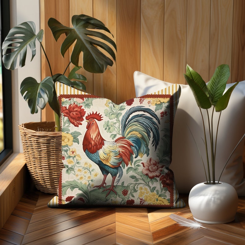 May include: A decorative throw pillow with a colorful rooster design on a white background. The rooster is surrounded by floral patterns in shades of red, yellow, green, and blue. The pillow is sitting on a wooden floor.