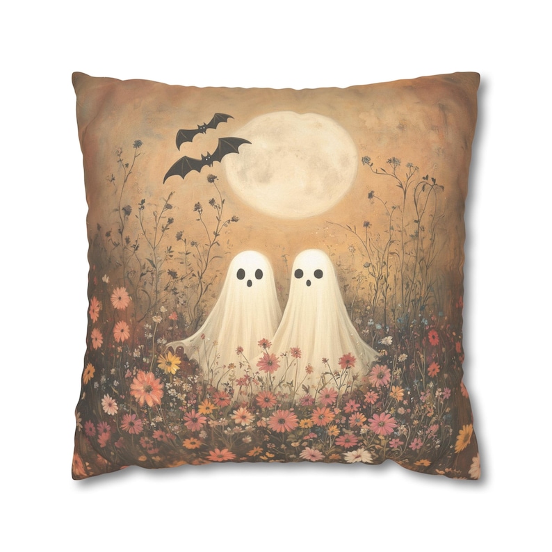 May include: Square throw pillow featuring a whimsical Halloween design. Two friendly ghost figures stand in a field of flowers under a full moon, with bats flying above. The color palette includes warm tones of orange, pink, and cream.