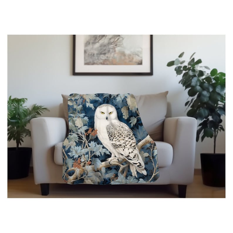 May include: A white snowy owl with yellow eyes perched on a branch with blue and green leaves. The owl is surrounded by a blue and green background with white flowers.