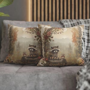 May include: Two decorative throw pillows with a woodland theme. The pillows feature a light brown background with a forest scene, including trees, leaves, and two raccoons. The raccoons are sitting on a log with a small owl perched on a branch nearby. The pillows are made of a soft, comfortable fabric and would be a great addition to any home.
