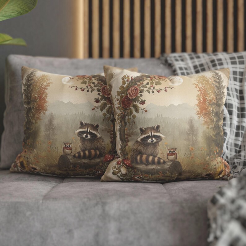 May include: Two decorative throw pillows with a woodland theme. The pillows feature a light brown background with a forest scene, including trees, leaves, and two raccoons. The raccoons are sitting on a log with a small owl perched on a branch nearby. The pillows are made of a soft, comfortable fabric and would be a great addition to any home.