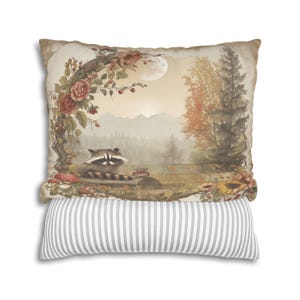 May include: A decorative throw pillow with a nature scene featuring a raccoon, a small owl, and a moon in a forest setting. The pillow has a gray and white striped back.