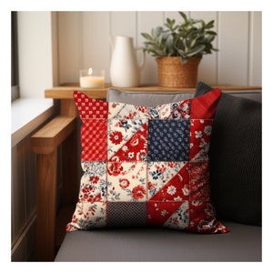 May include: Red, white, and blue patchwork pillow with a floral pattern. The pillow is made of different fabrics and has a square shape.